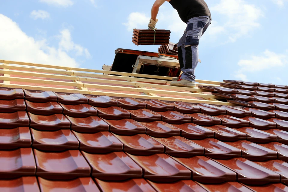 Ouvrier couvreur en tenue blanche installant des tuiles terre cuite sur une toiture en construction sous ciel bleu dégagé