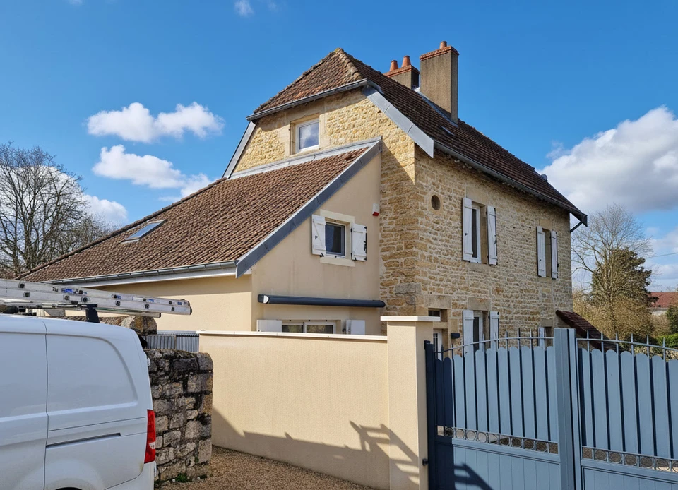 Un ouvrier en v&ecirc;tements sombres et gants orange installe un bardage bois vertical sur la fa&ccedil;ade ext&eacute;rieure d'une maison moderne