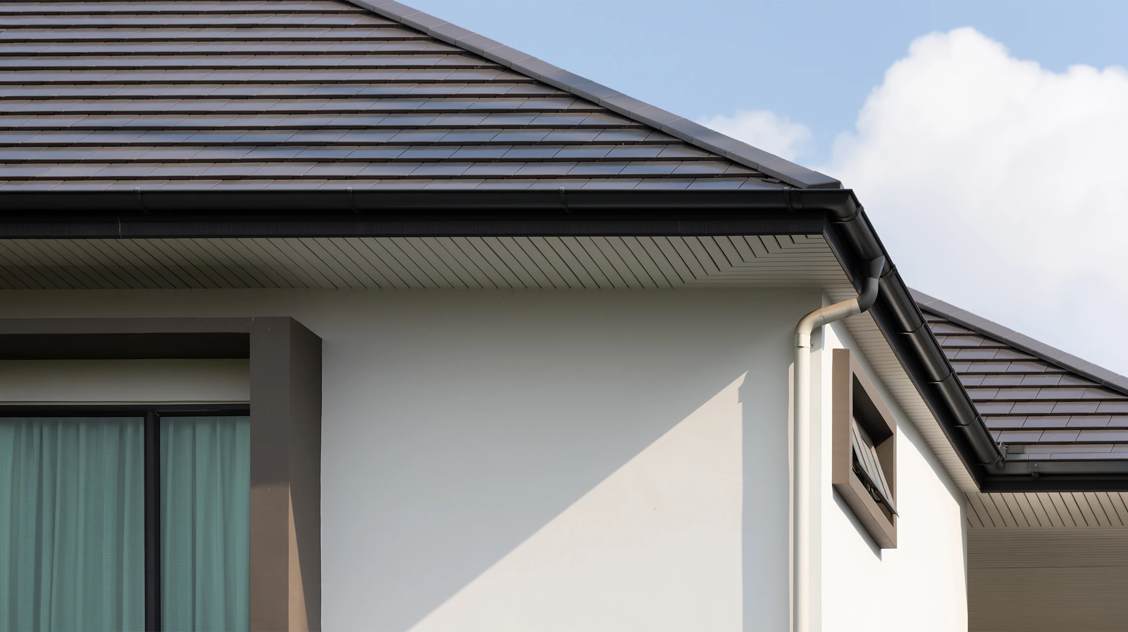 Ouvrier installant une gouttière sur le toit d'une maison résidentielle à bardage bois