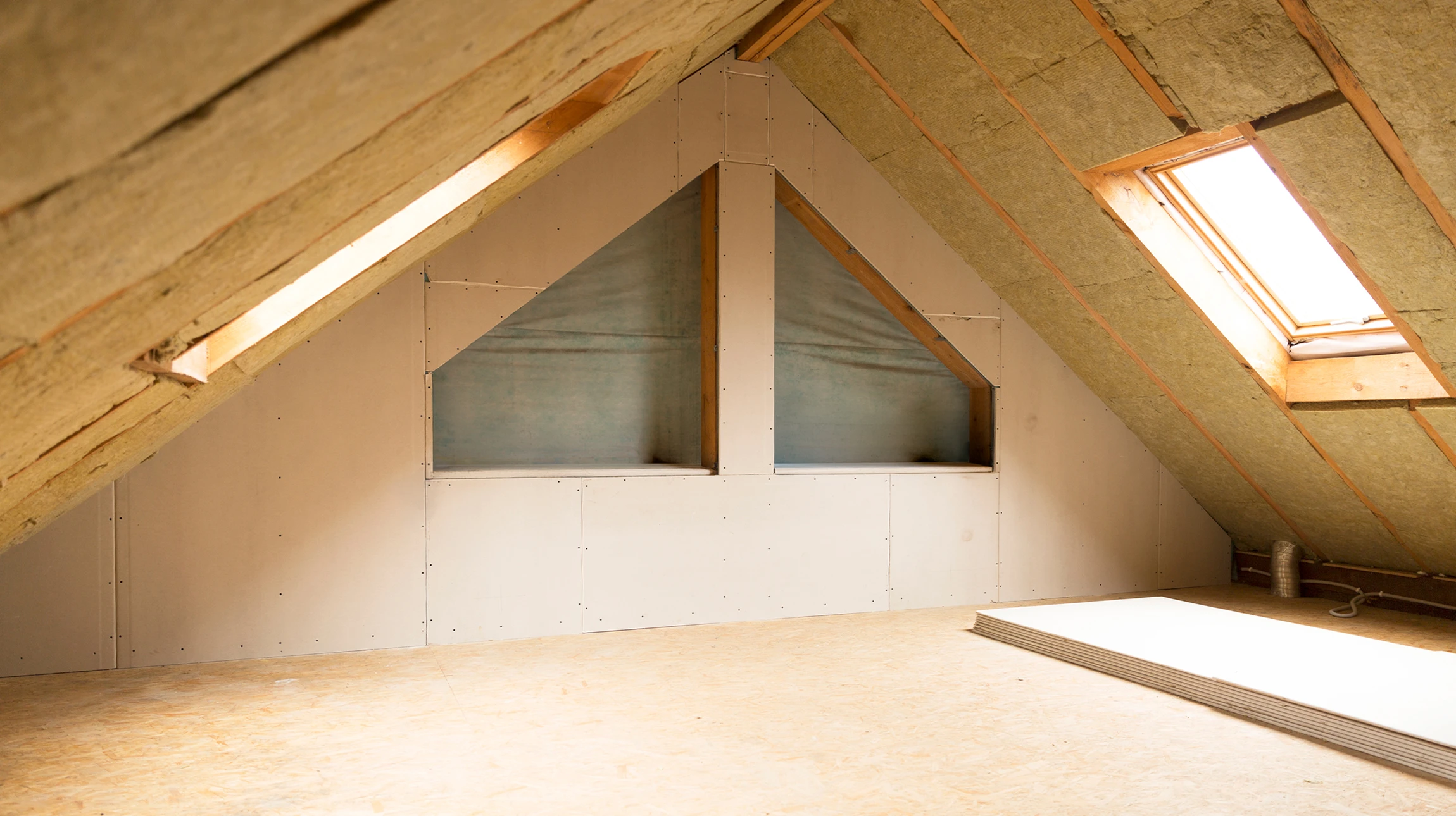 Ouvrier installant des panneaux d'isolation de laine minérale dans le toit de la maison