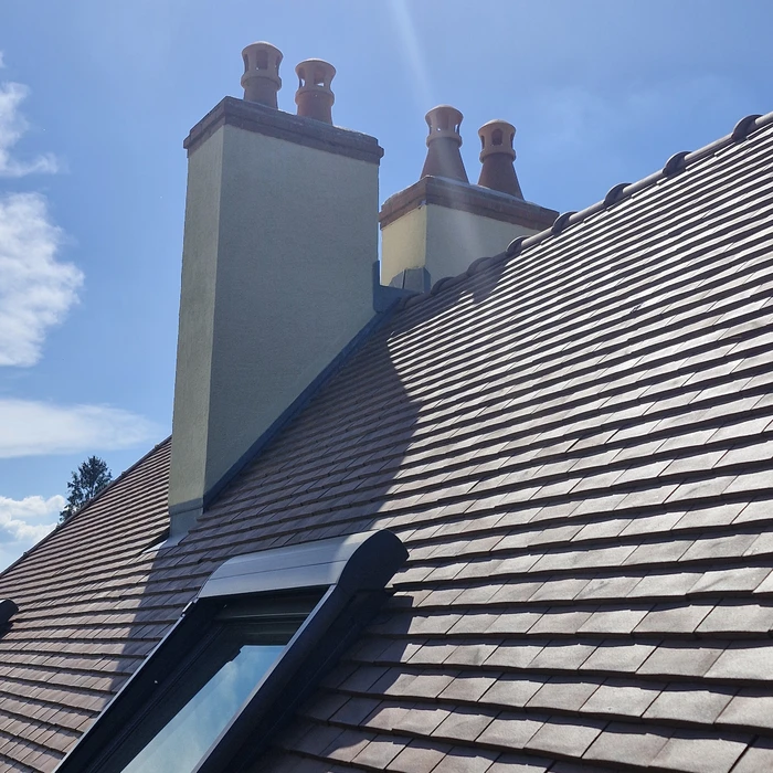 Deux couvreurs travaillant sur une toiture en pente, installant des tuiles terre cuite rouge