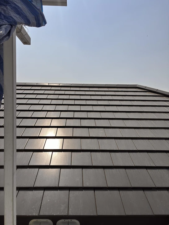 Ouvrier couvreur installant des tuiles terre cuite rouge sur charpente bois, travaux de toiture en cours sous ciel bleu